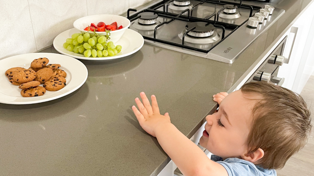 Child reaching for biscuits on bench.